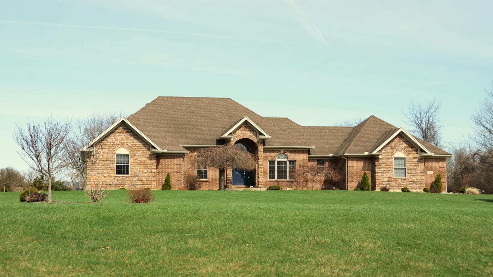 Large brick ranch-style home with brown shingle roof on a wide green lawn
